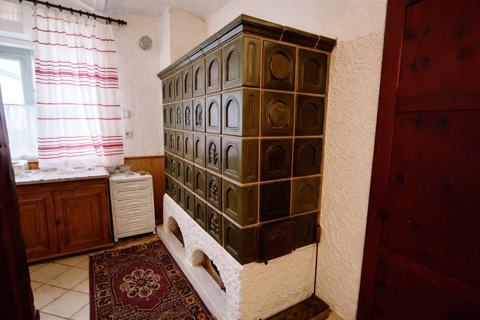 Ein traditioneller grüner Kachelofen in einem Raum mit Teppich und Fenster.