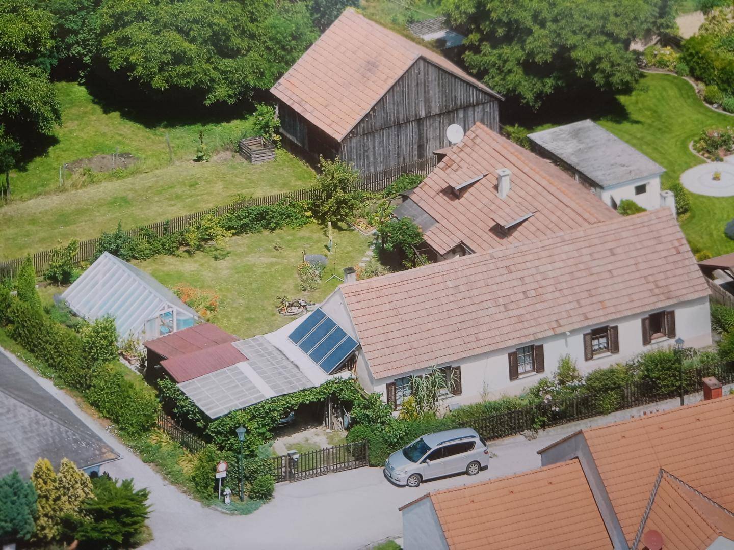 Luftaufnahme des Anwesens mit mehreren Gebäuden, Garten und Gewächshaus.