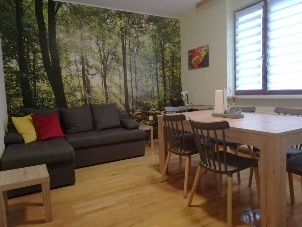 Heller Wohn-Essbereich mit Sofa, Esstisch und einer großen Waldtapete als Akzentwand.