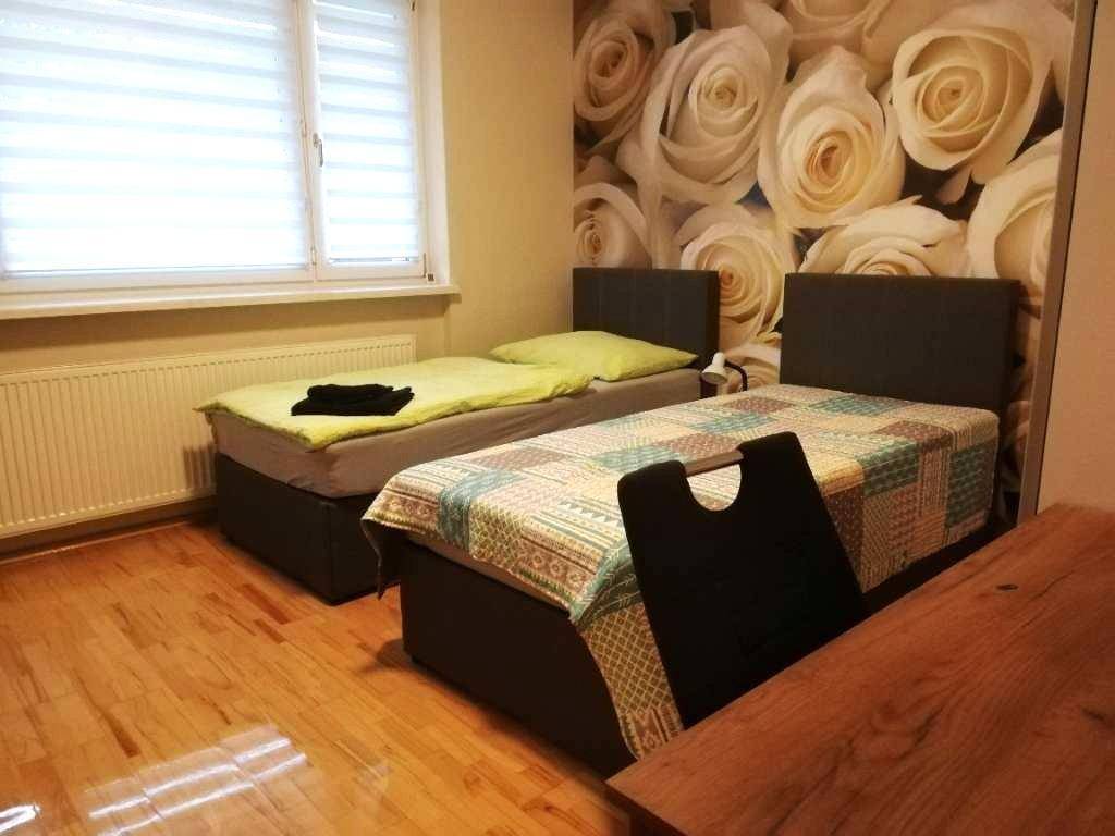 Schlafzimmer mit zwei Einzelbetten, Holzboden und einer Wandtapete mit Rosenmotiv.