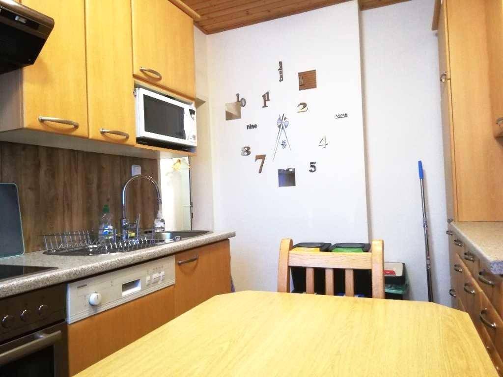 Kleine Küche mit Holzschränken, Esstisch und einer großen Wanduhr als Dekoration.