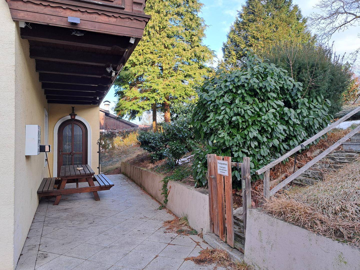Außenbereich mit gepflasterter Terrasse, Picknicktisch und einem grünen, leicht geneigten Garten.