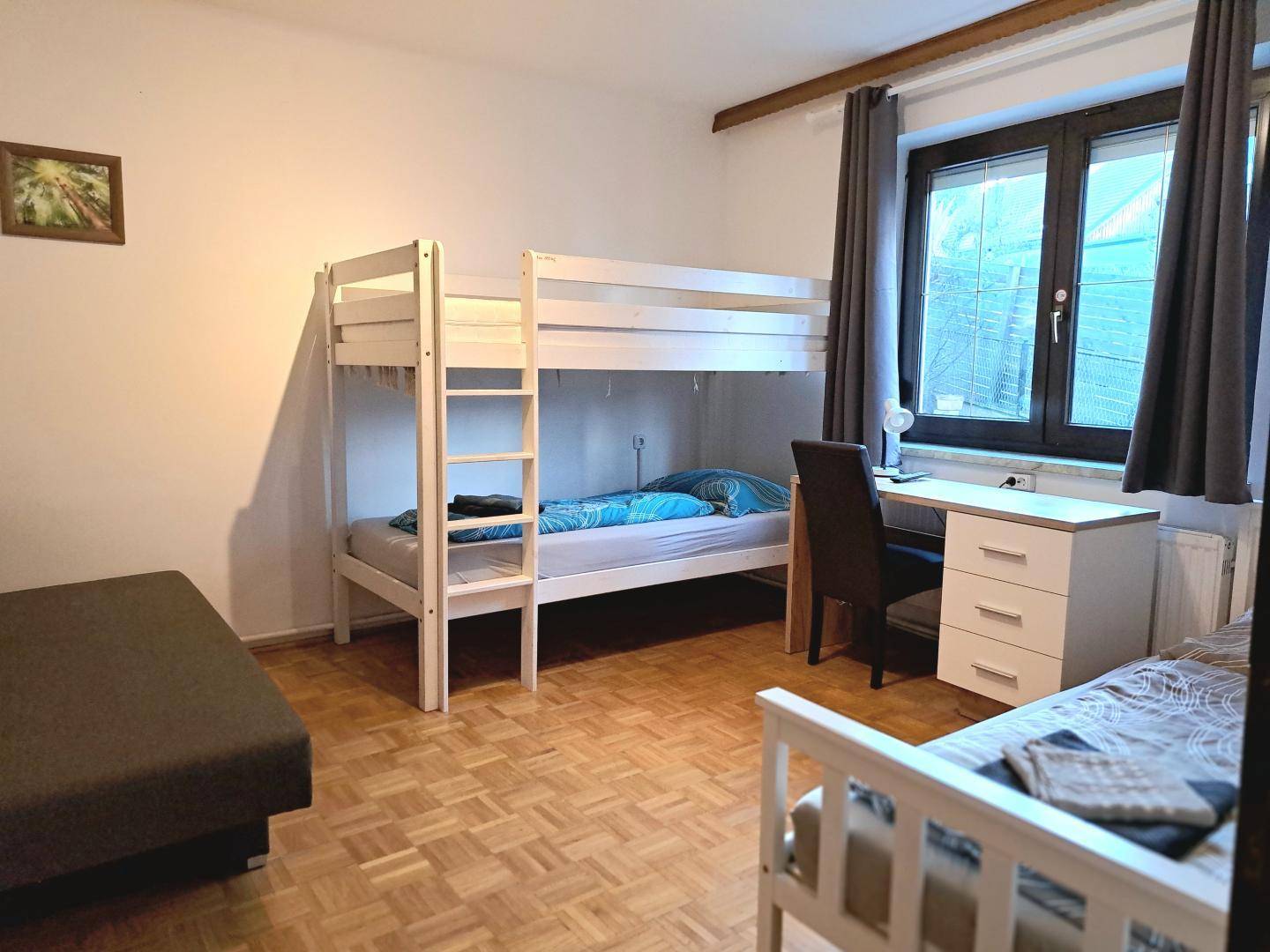 Helles Schlafzimmer mit Etagenbett, Einzelbett und Schreibtisch, ideal für Gäste oder Kinder.