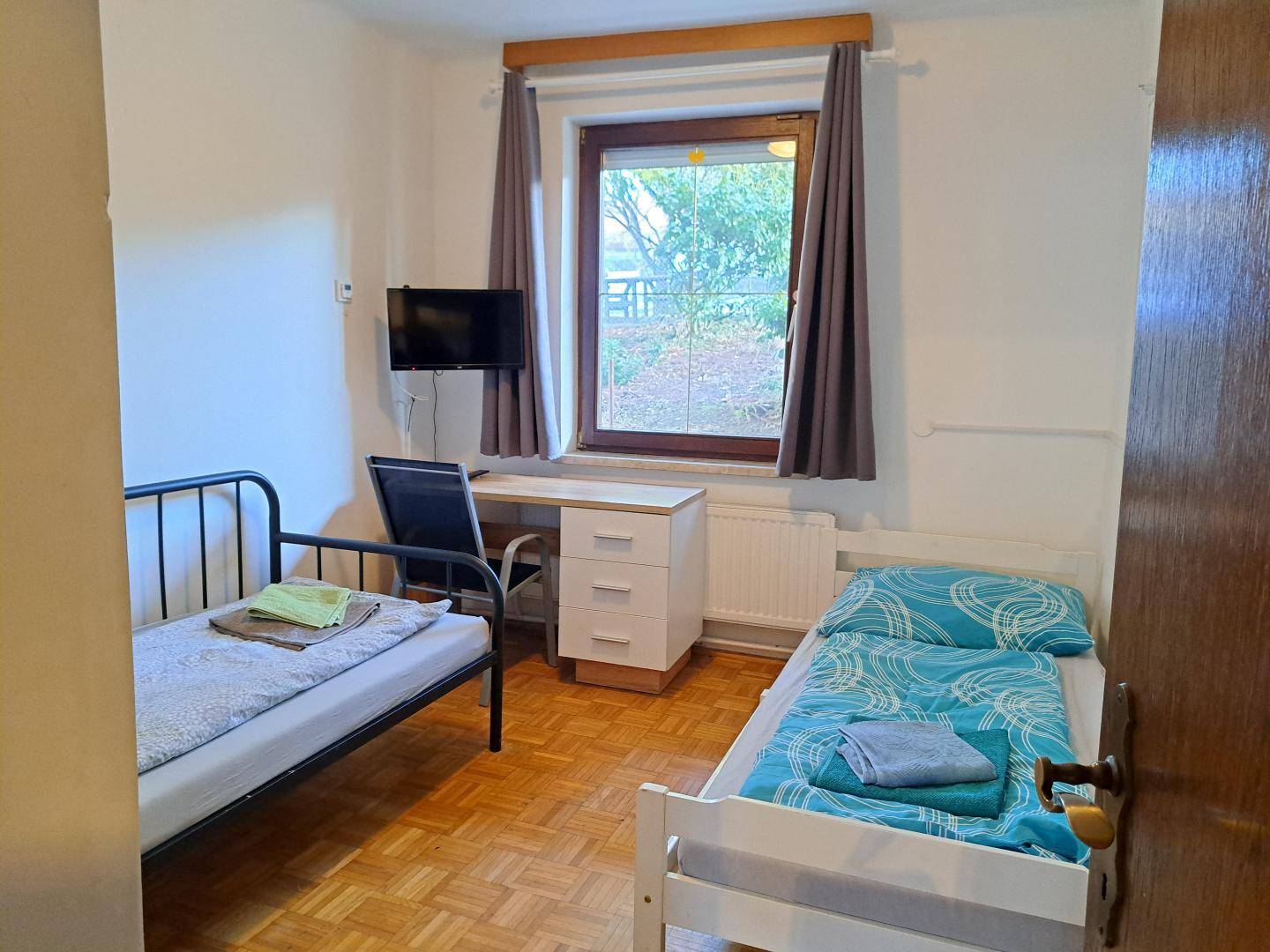 Gemütliches Schlafzimmer mit zwei Einzelbetten, Schreibtisch und Fernseher, mit Blick ins Grüne.