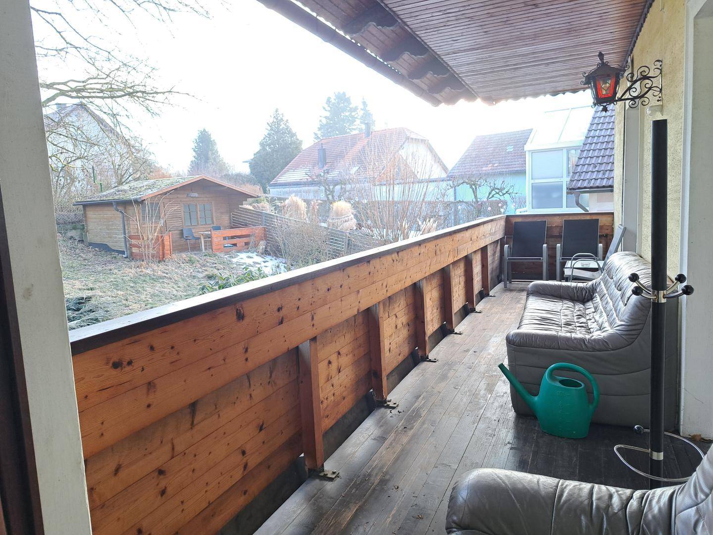 Großer Holzbalkon mit Sitzgelegenheiten und Blick auf den Garten und die Umgebung.