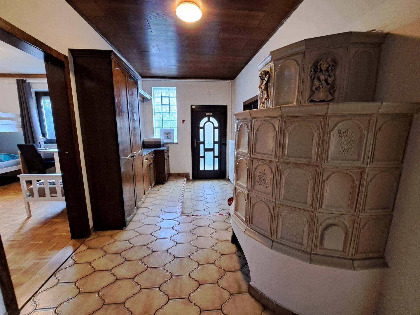 Geräumiger Flur mit traditionellem Kachelofen, Holzdecken und Zugang zu weiteren Zimmern.