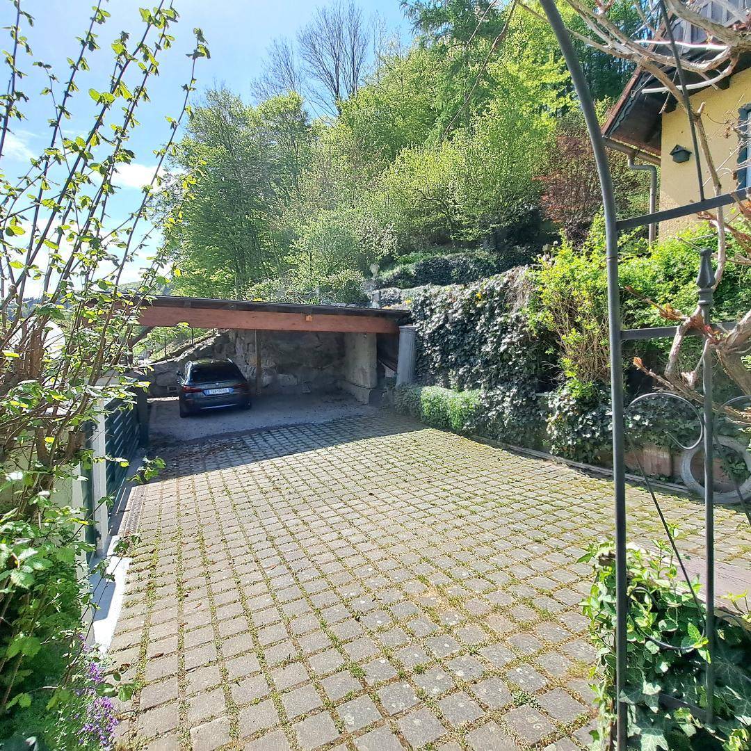 Gepflasterte Einfahrt mit überdachtem Stellplatz und grüner Hanglage.