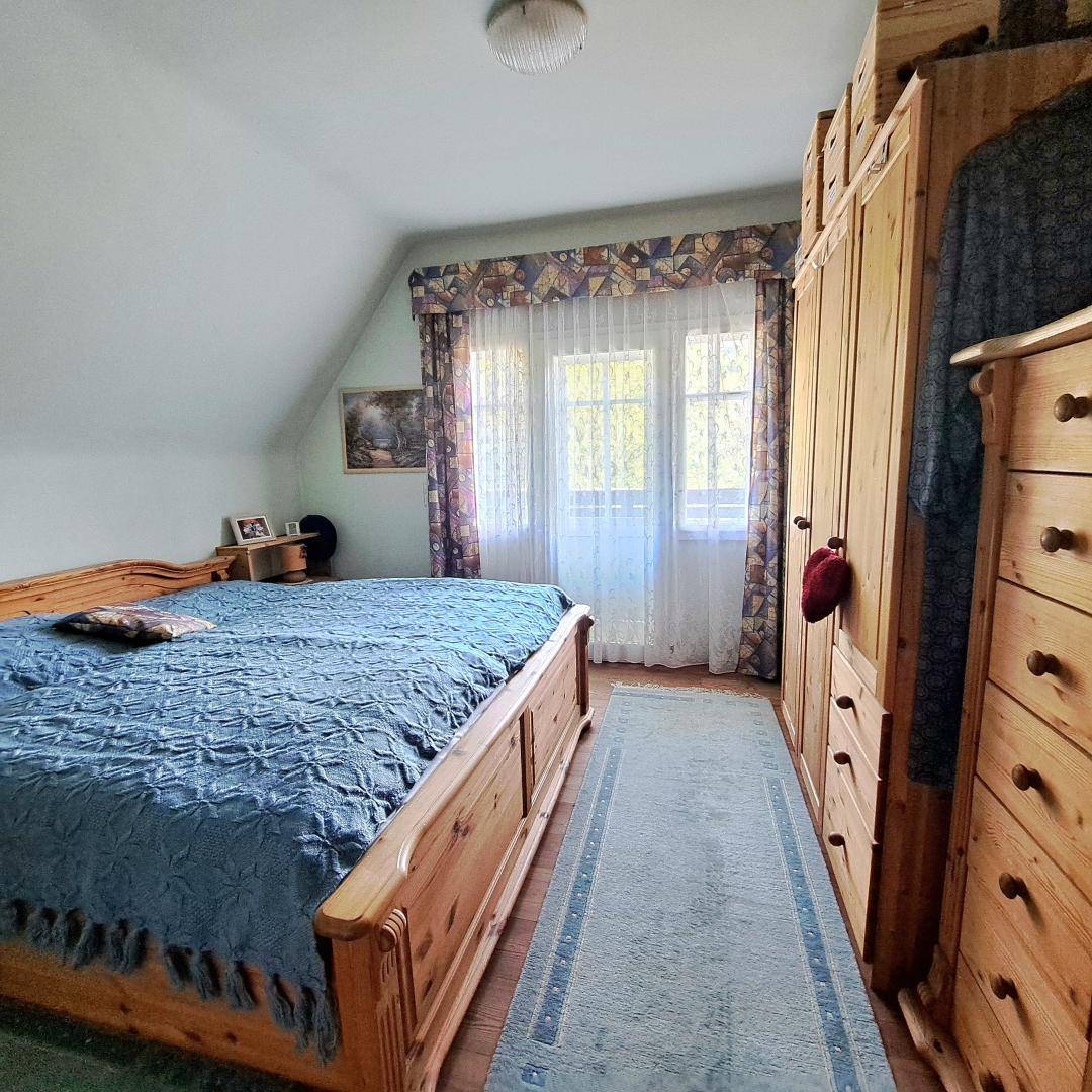 Schlafzimmer mit Holzbett, Kleiderschrank und Dachschräge, hell durch Fenster.
