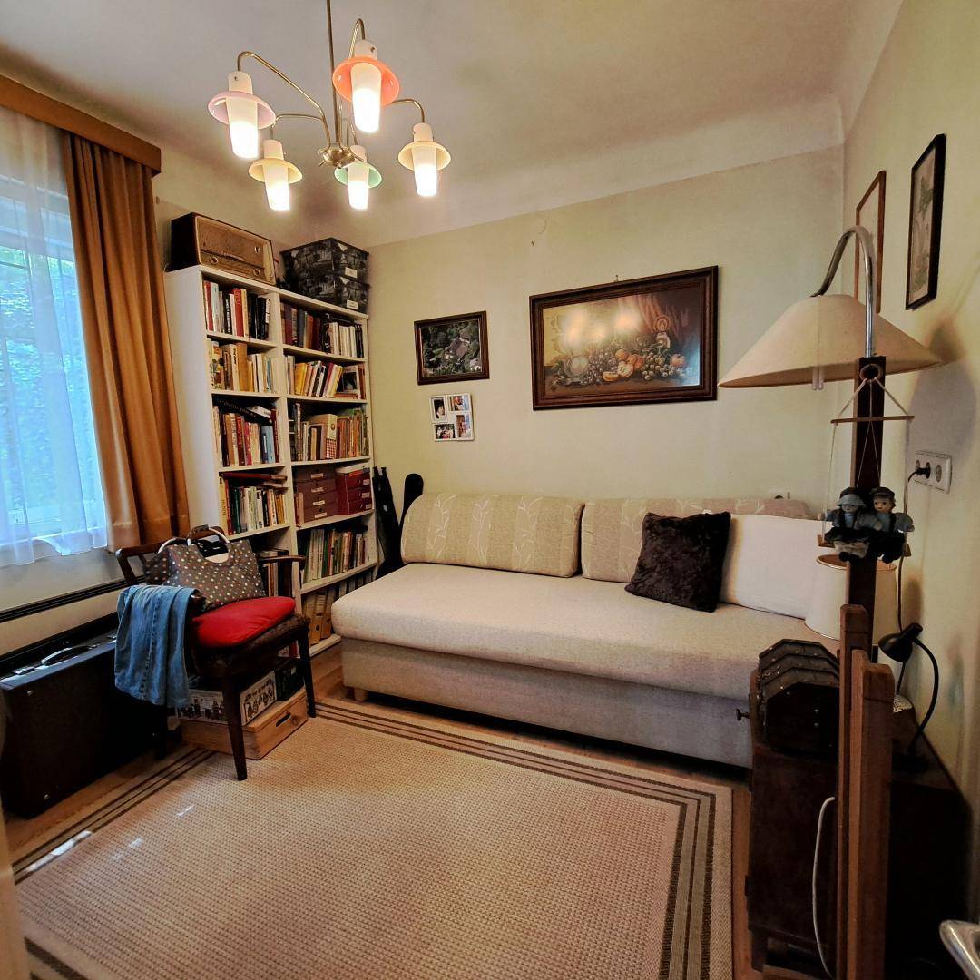 Helles Zimmer mit Schlafsofa, Bücherregal und Fenster für natürliches Licht.