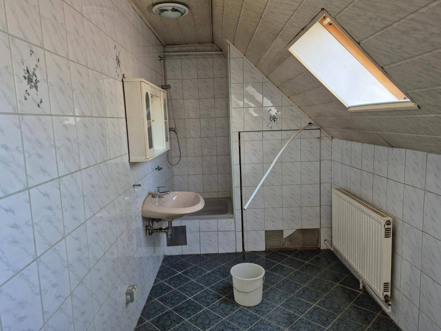Gefliestes Badezimmer im Dachgeschoss mit Schrägen, Waschbecken und Dusche.