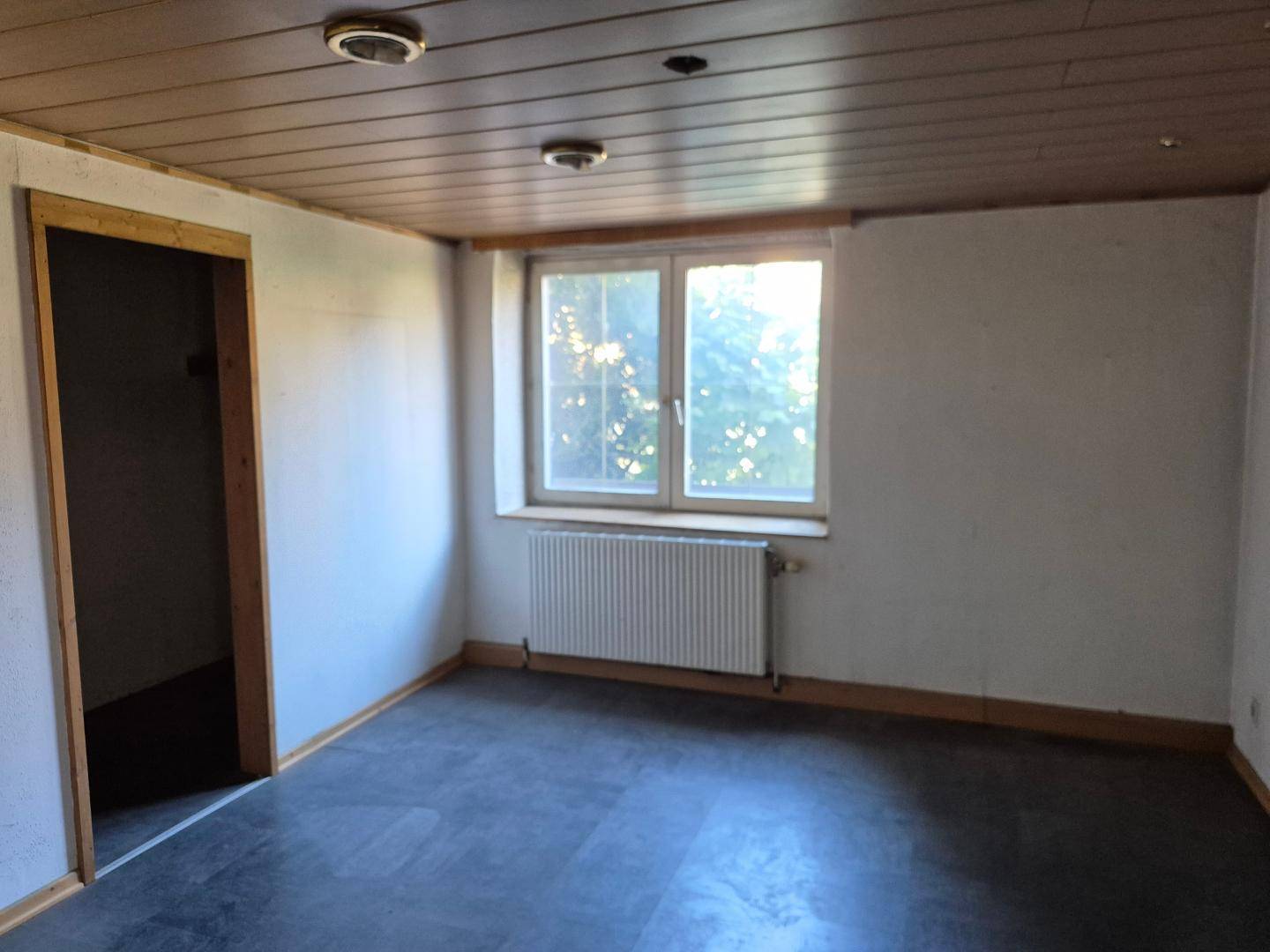 Schlafzimmer mit dunklem Boden, Fenster und Heizkörper, bereit zur individuellen Gestaltung.