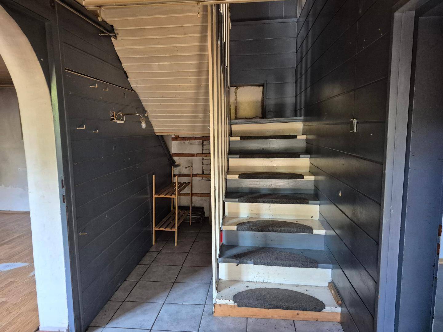 Treppenhaus mit Holzverkleidung und gefliestem Boden, führt in die obere Etage.