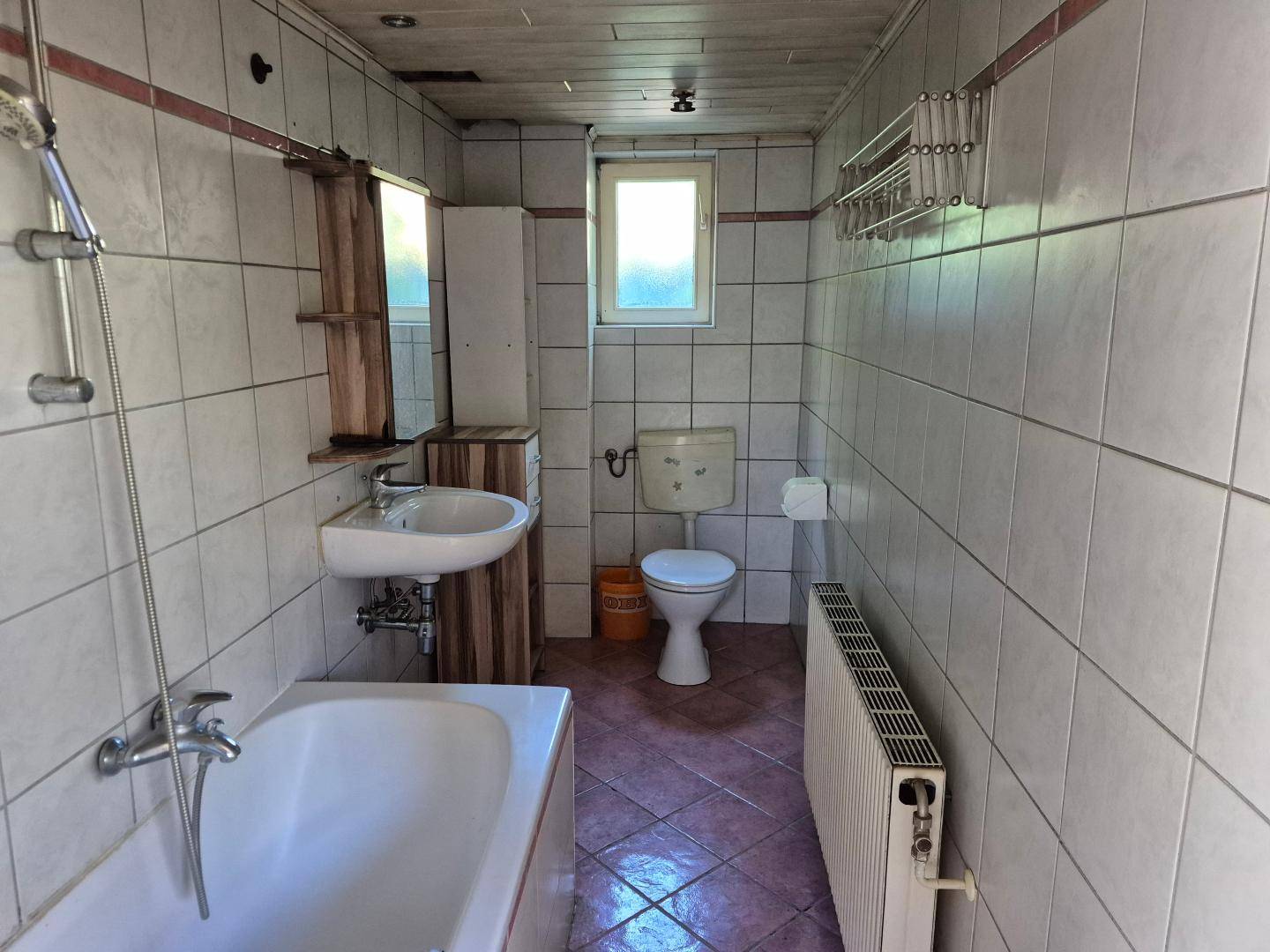 Gefliestes Badezimmer mit Badewanne, Waschbecken und WC, in einfachem Zustand.