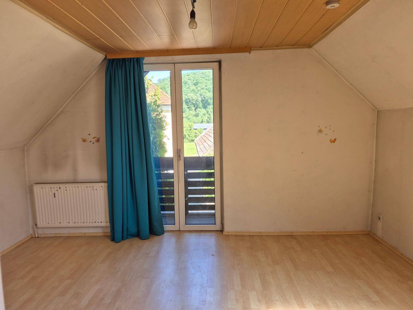 Helles Zimmer im Dachgeschoss mit Balkonzugang und Holzboden.