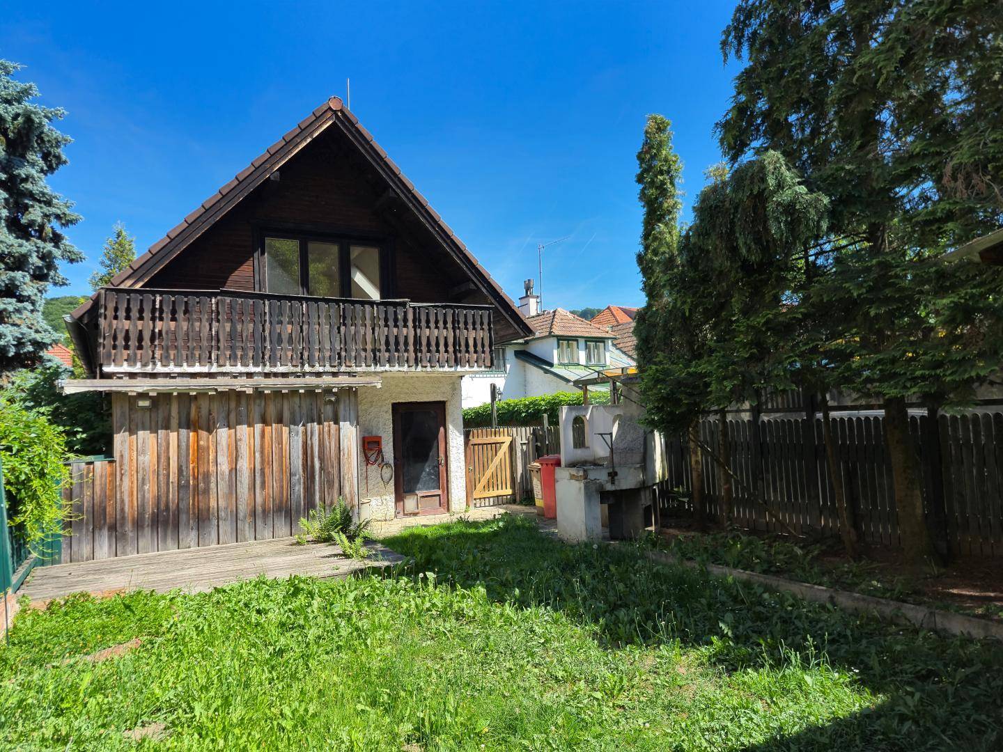 Hinterhof mit Rasenfläche, Holzfassade und Balkon, umgeben von Bäumen.