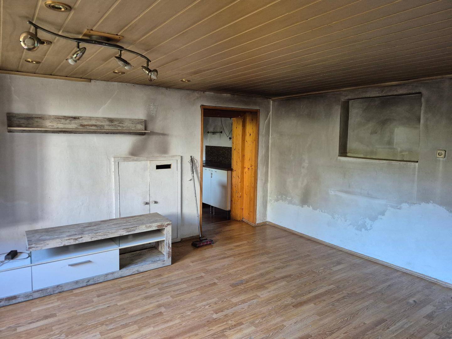 Unfertiger Wohnraum mit Holzdeckenverkleidung und Laminatboden, bereit für die Renovierung.