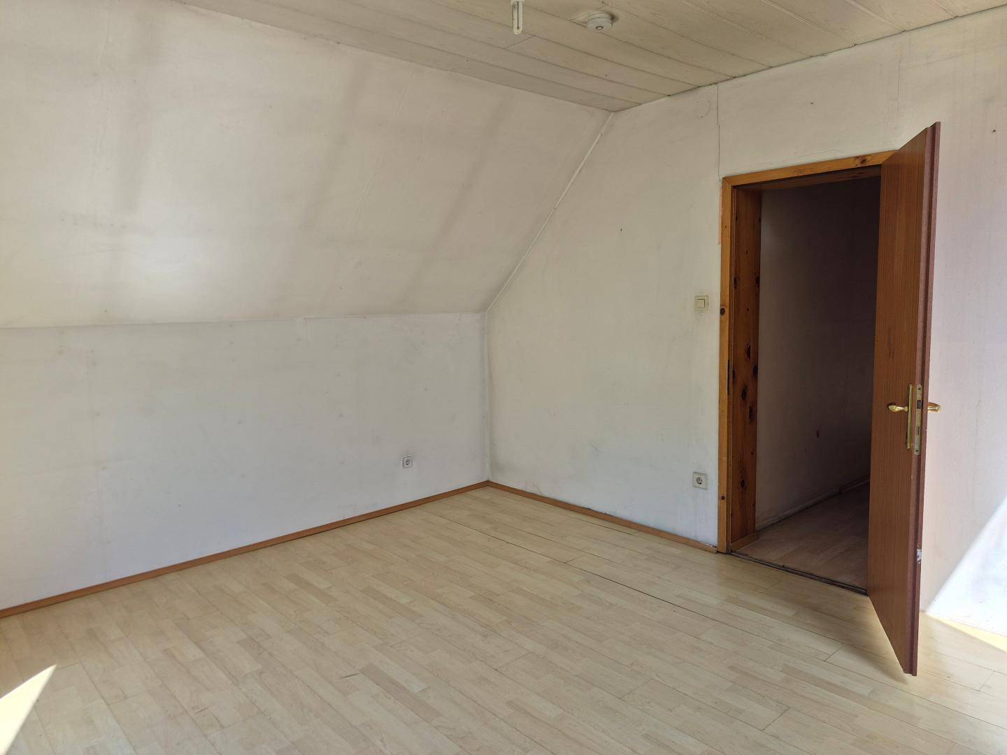 Geräumiges Zimmer im Dachgeschoss mit Schrägen und Holzboden, ideal für individuelle Nutzung.