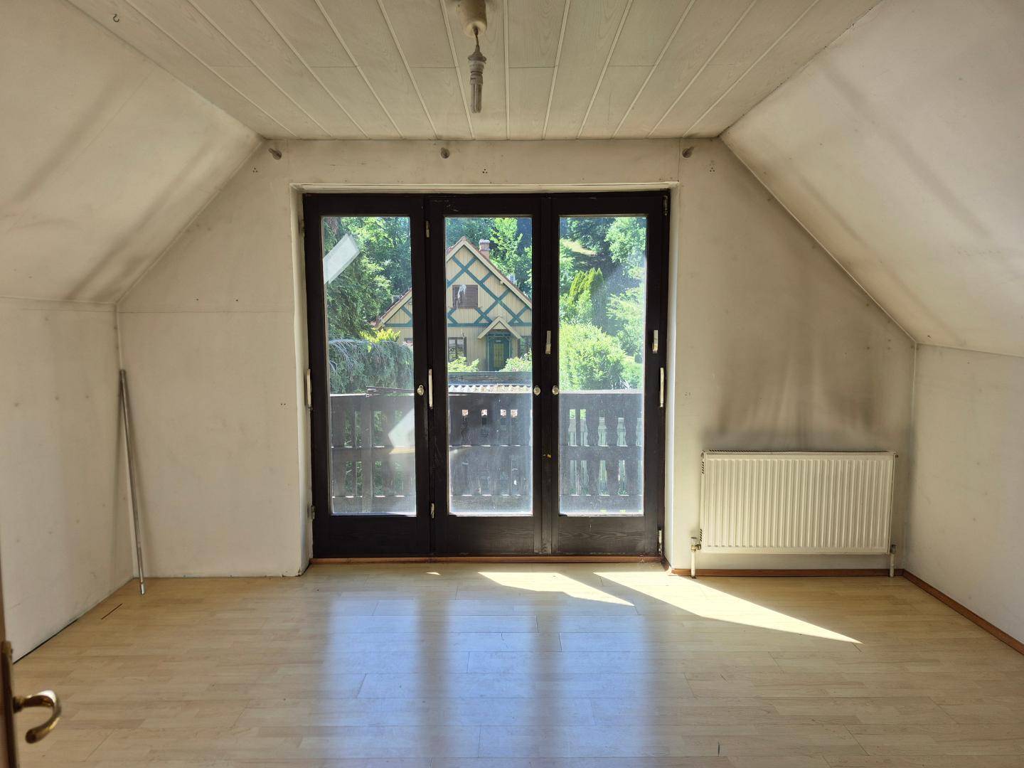 Helles Zimmer im Dachgeschoss mit Balkonzugang und Holzboden.