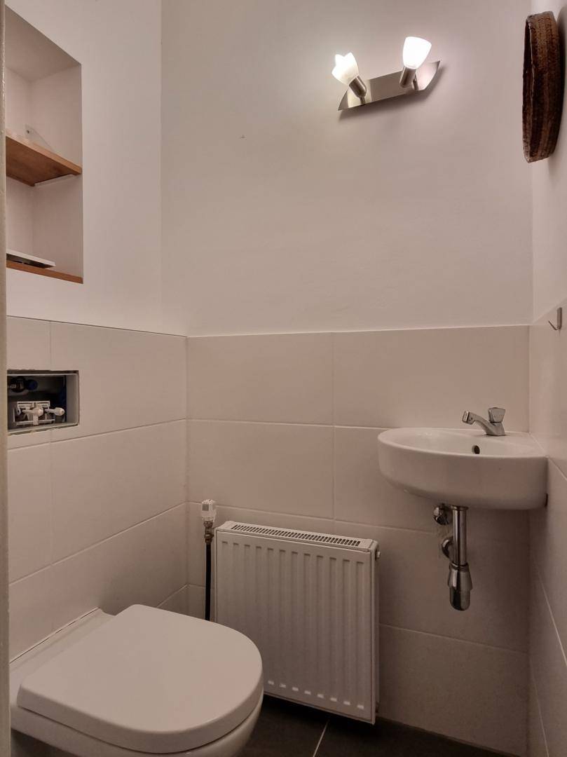 Modernes Gäste-WC mit wandhängender Toilette, kleinem Waschbecken und weißen Fliesen.