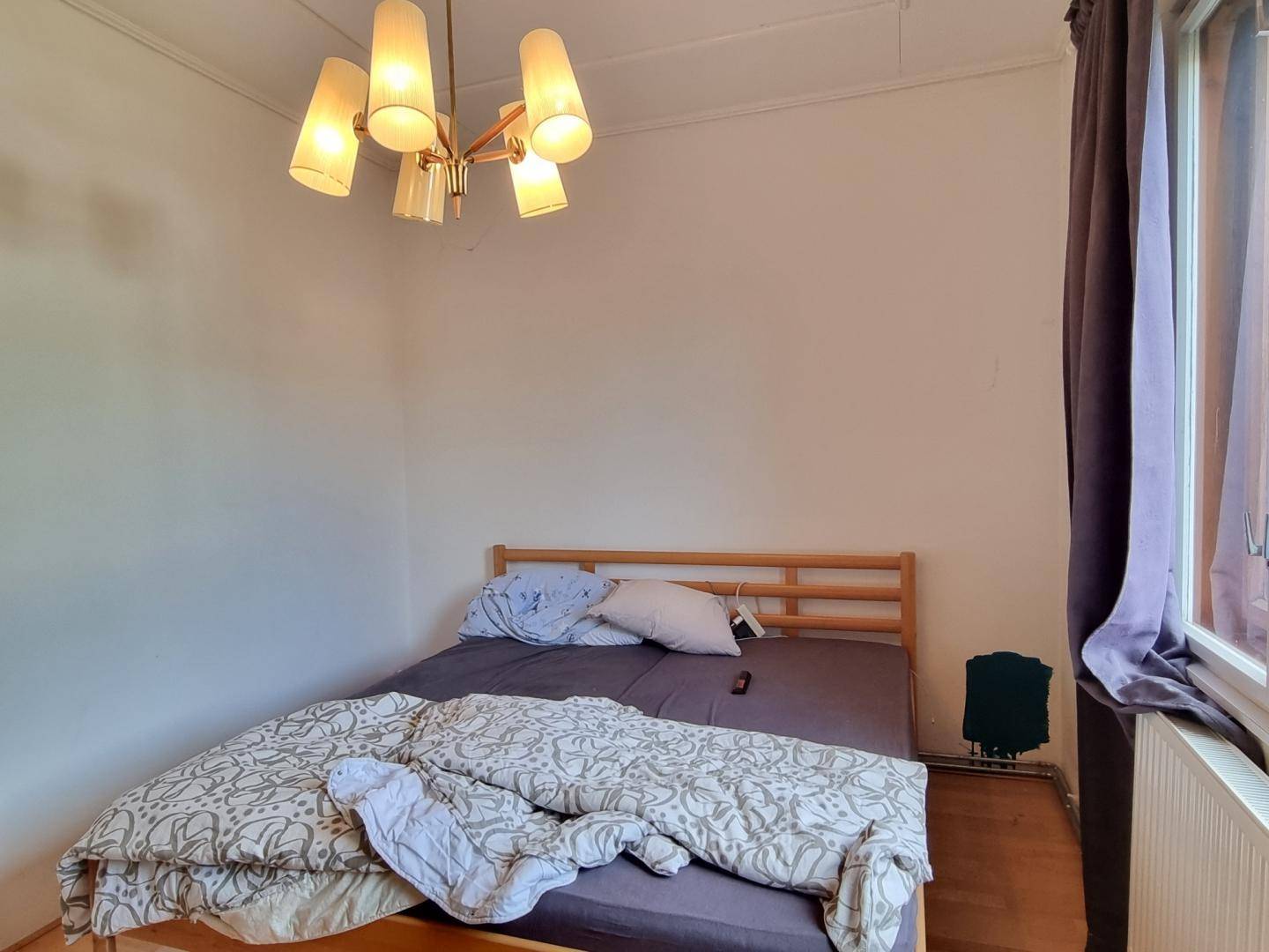 Schlafzimmer mit Holzbett, Parkettboden und einem Fenster, das Tageslicht hereinlässt.
