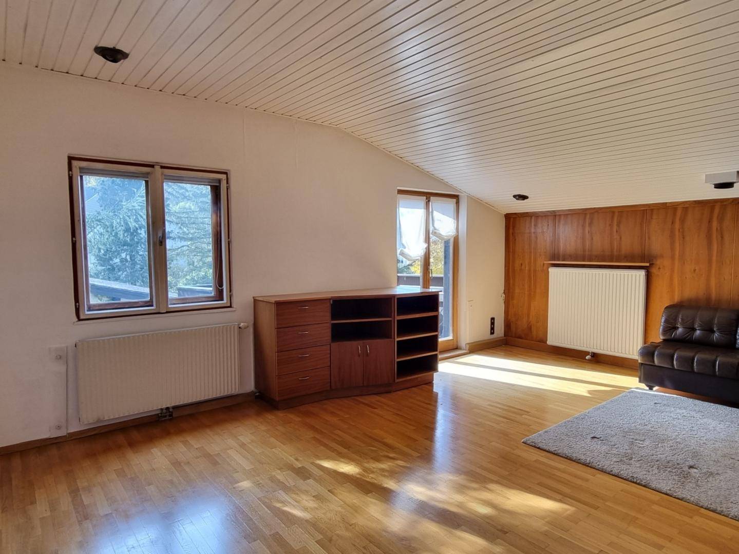Helles Wohnzimmer im Dachgeschoss mit Holzboden, Holzvertäfelung und Zugang zum Balkon.