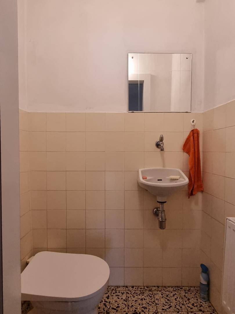 Kleines Gäste-WC mit beigefarbenen Fliesen, Waschbecken und Spiegel.