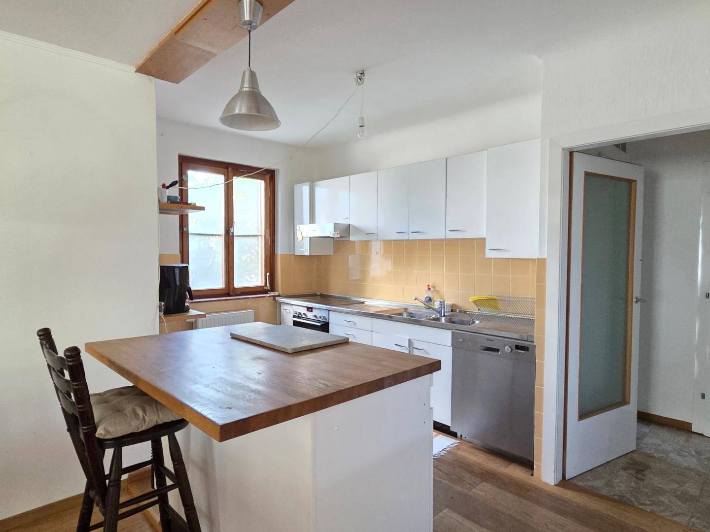 Funktionale Küche mit weißen Schränken, Holztheke und gelben Fliesen, bereit zur Modernisierung.