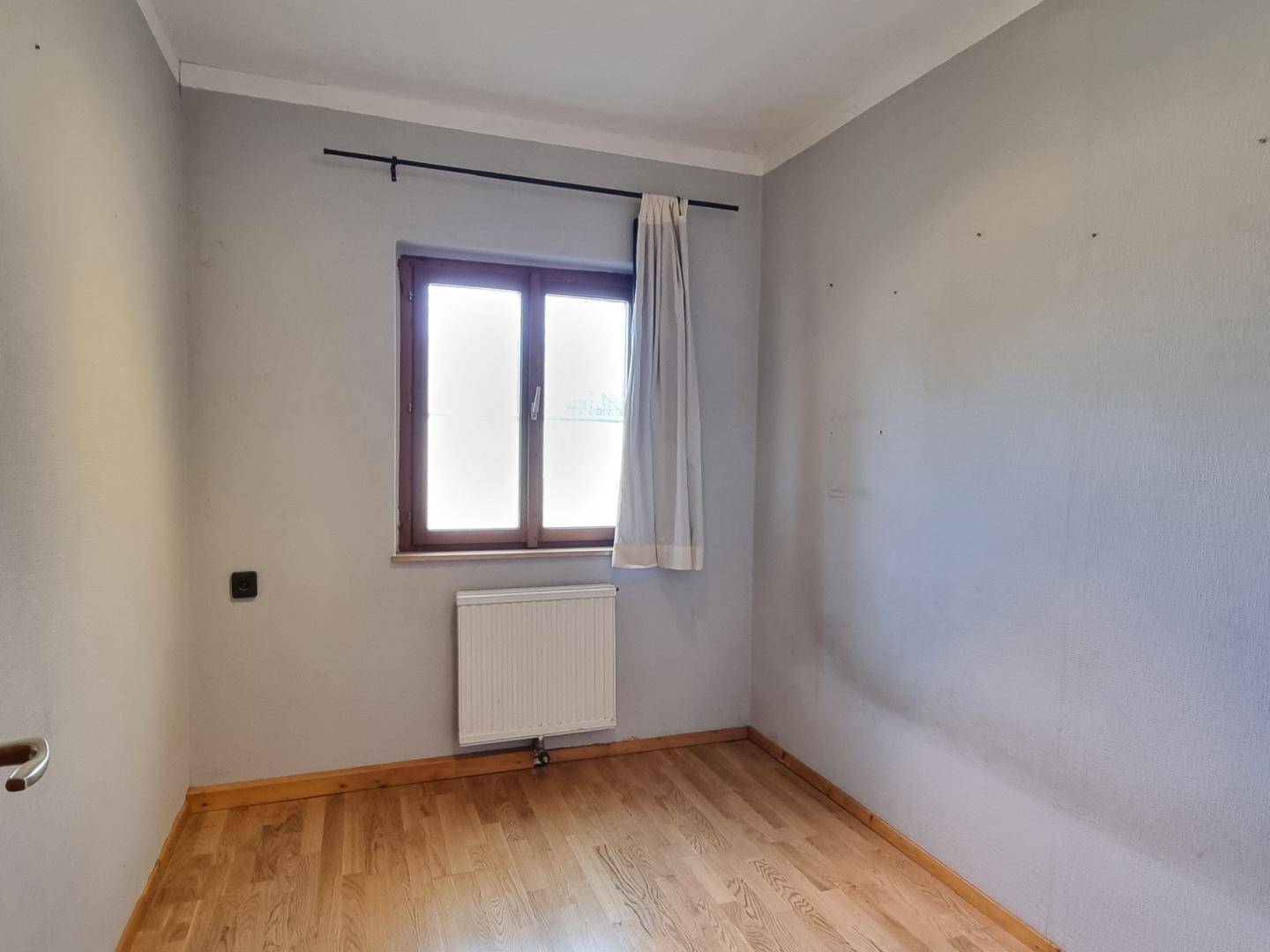 Kleines Schlafzimmer mit Holzboden, Fenster und Heizkörper, ideal als Kinderzimmer.