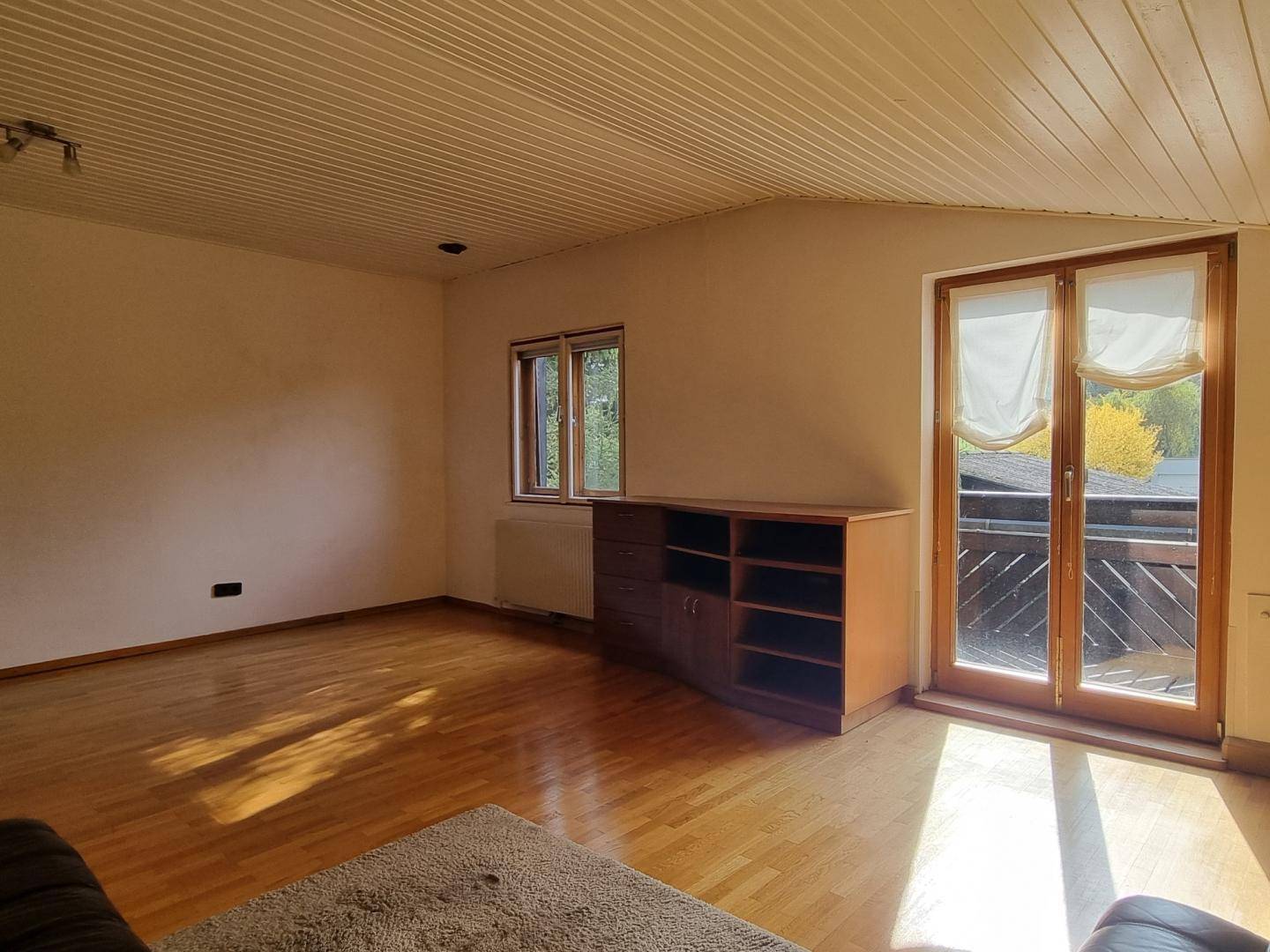 Lichtdurchflutetes Wohnzimmer mit Holzboden, Dachschrägen und Balkontür.