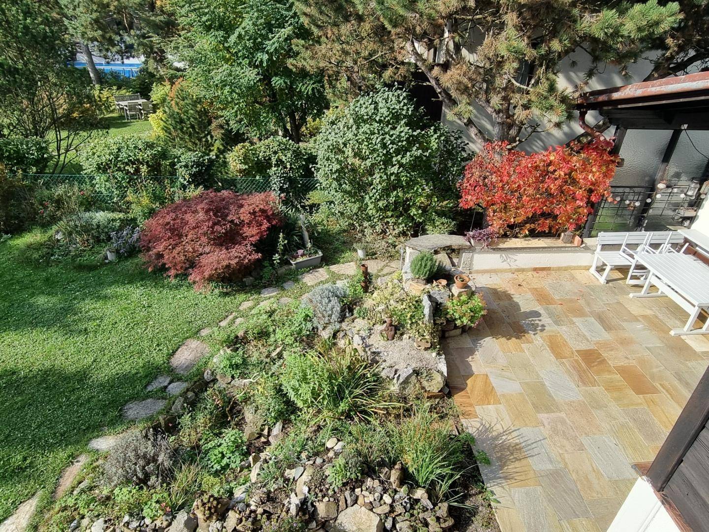 Weitläufiger Garten mit Terrasse, üppiger Bepflanzung und Blick auf die Umgebung.