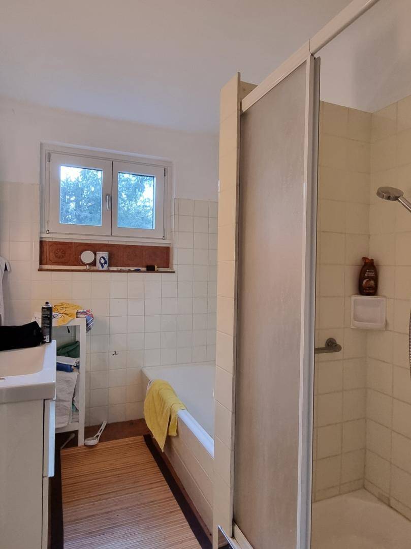 Badezimmer mit Badewanne, Duschkabine und Fenster, gefliest in hellem Beige.