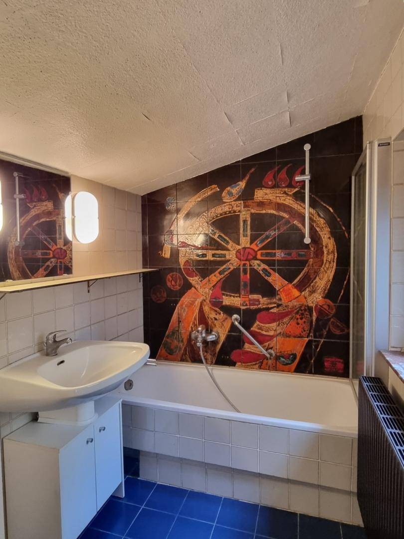 Badezimmer mit Badewanne, Duschvorrichtung und auffälliger Wandfliesenkunst.