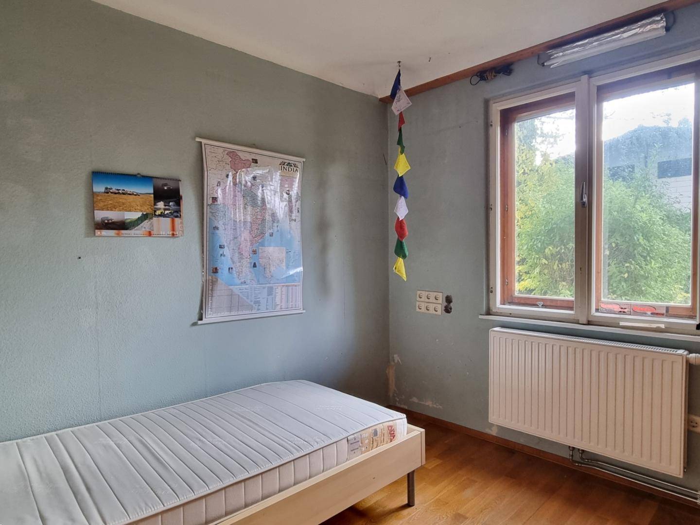 Schlafzimmer mit Einzelbett, hellblauen Wänden und Fenster mit Blick ins Grüne.