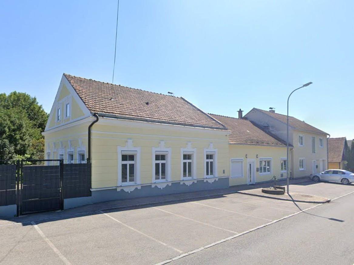 Gelbes Haus mit traditionellem Ziegeldach und Parkplätzen an einer ruhigen Straße.