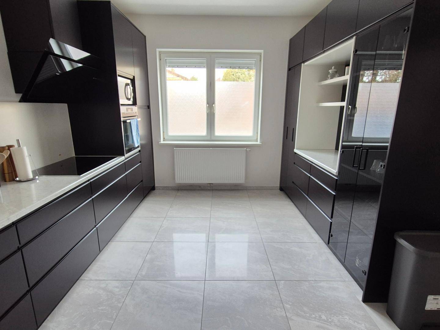 Moderne schwarze Küche mit glänzenden Fronten, Fliesenboden und integrierten Geräten.