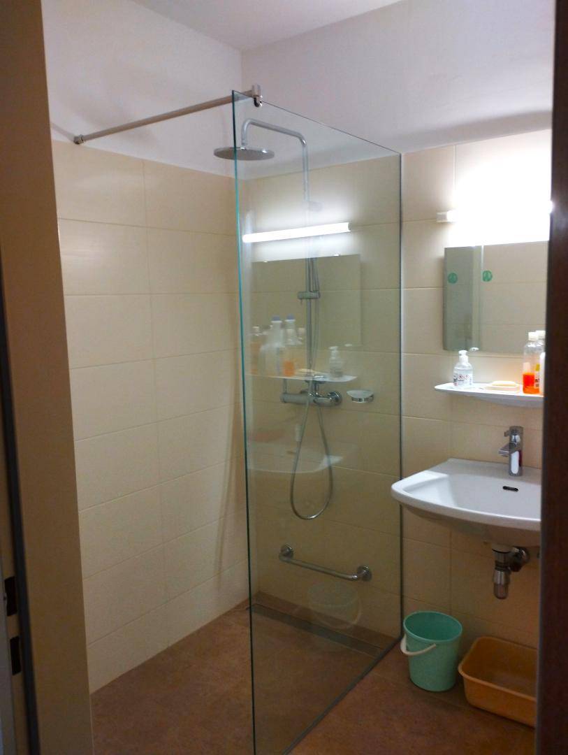 Modernes Badezimmer mit begehbarer Dusche, einzelnen Waschbecken und beigen Fliesen.