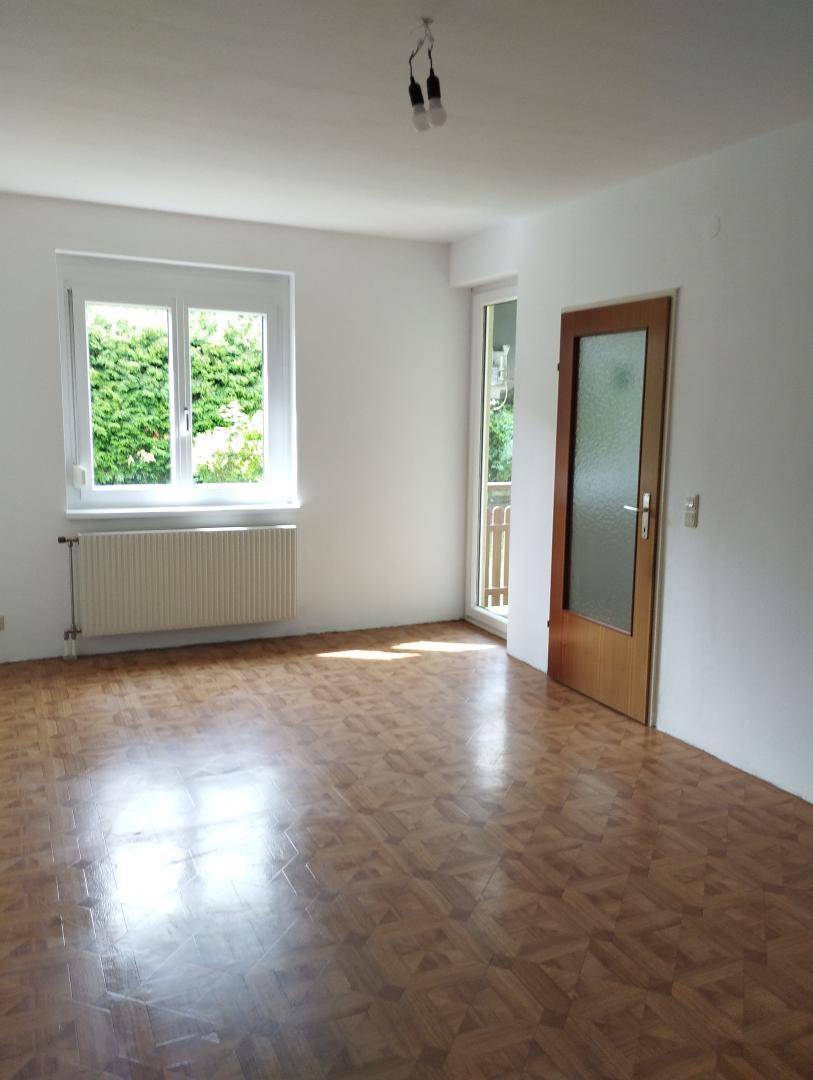 Heller Raum mit Parkettboden, Zugang zum Balkon und Ausblick ins Grüne.
