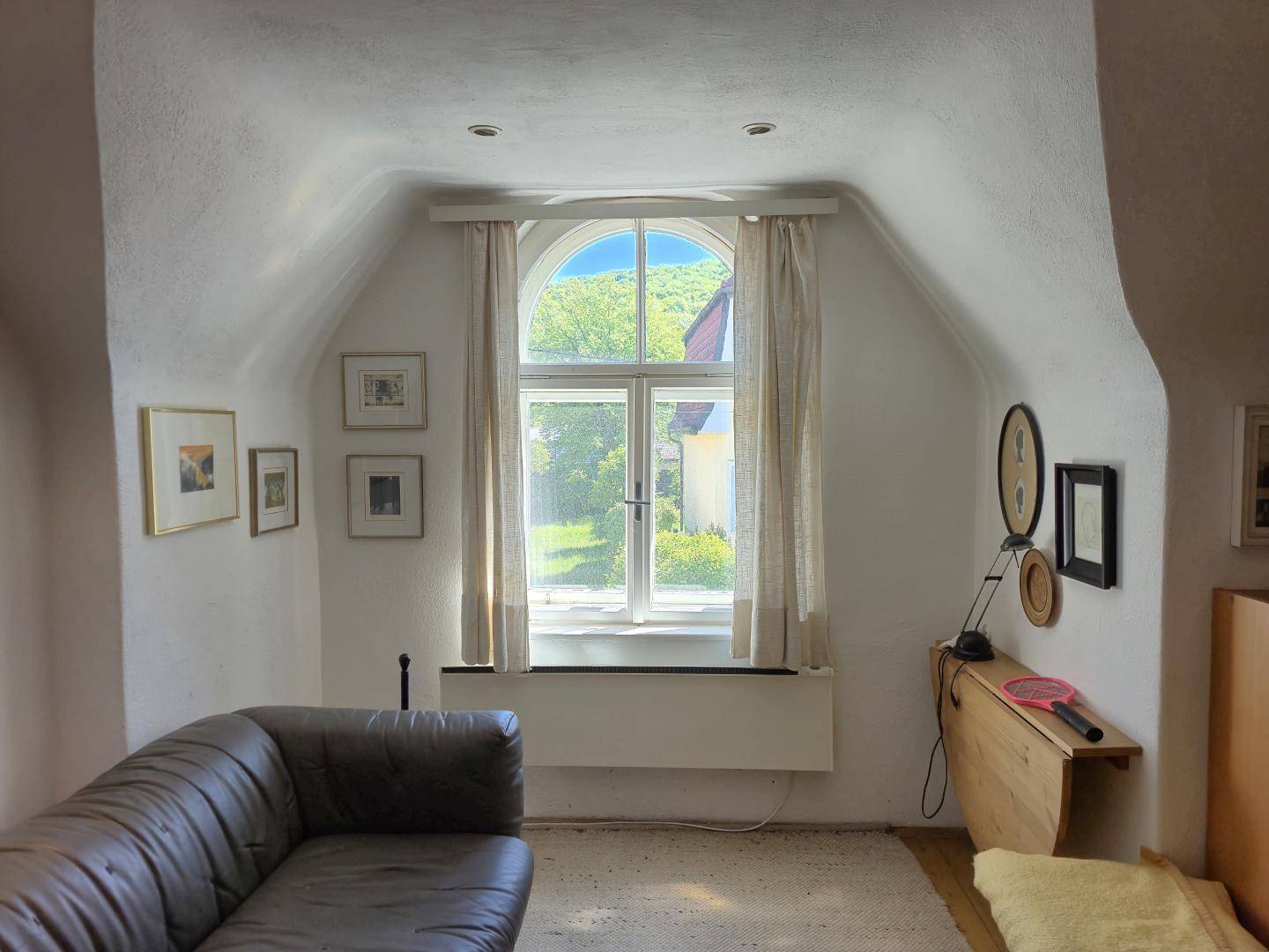 Gemütlicher Wohnbereich mit gewölbter Decke, Sofa und einem großen Fenster mit Blick ins Grüne.