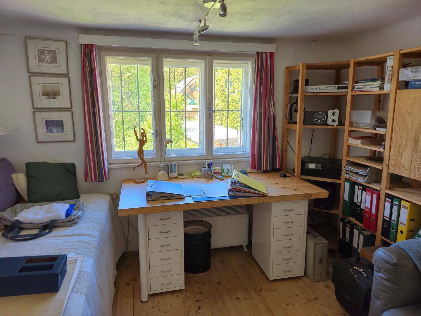 Helles Arbeitszimmer mit Schreibtisch, Bücherregalen und Blick ins Grüne durch die Fenster.