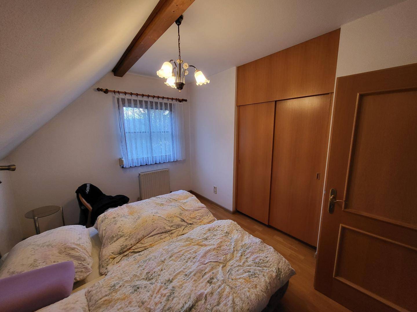 Schlafzimmer im Dachgeschoss mit Holzbalken, Einbauschränken und Fenster.