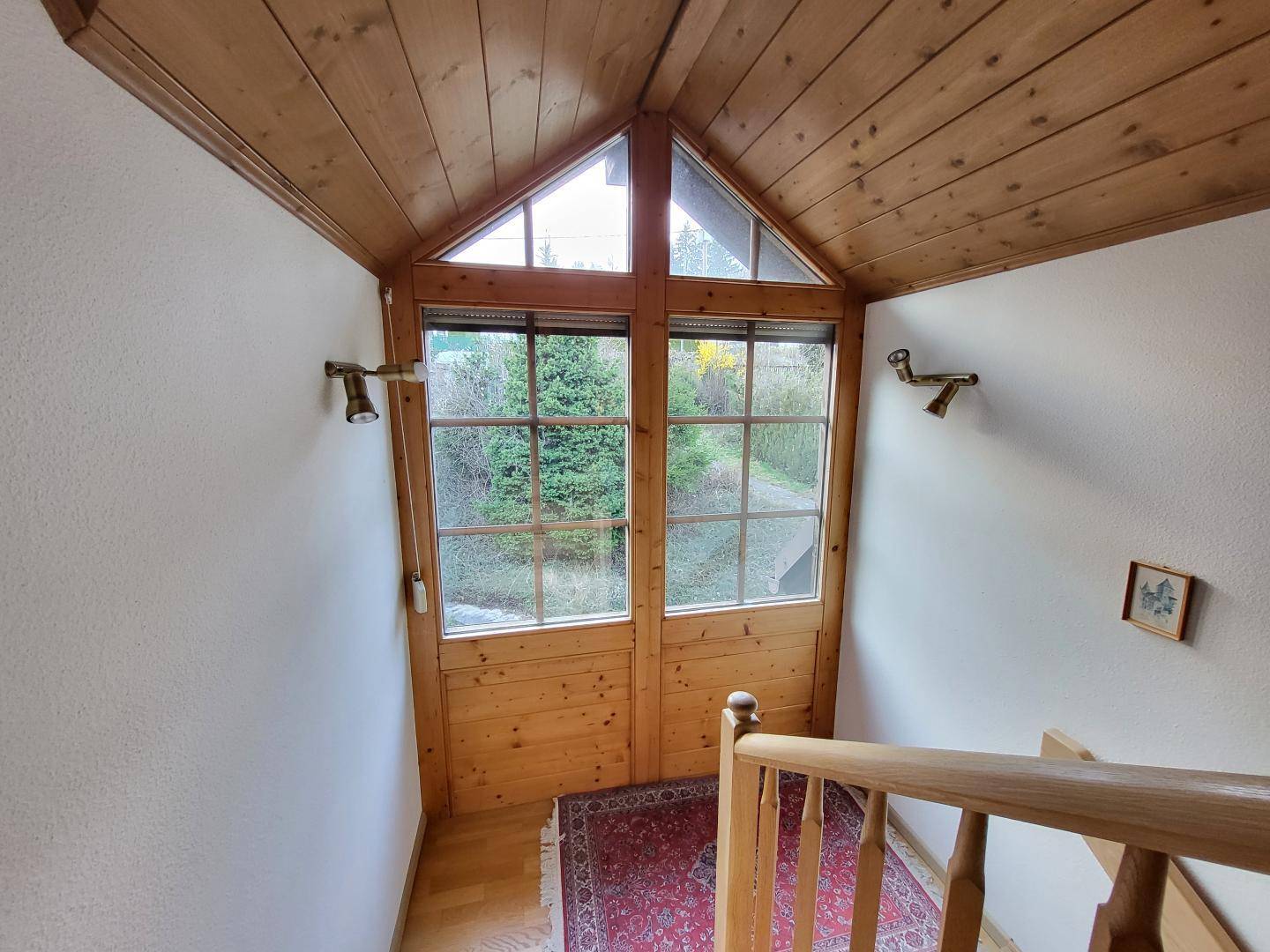 Treppenaufgang mit Holzverkleidung und großen Fenstern, die den Blick ins Grüne freigeben.
