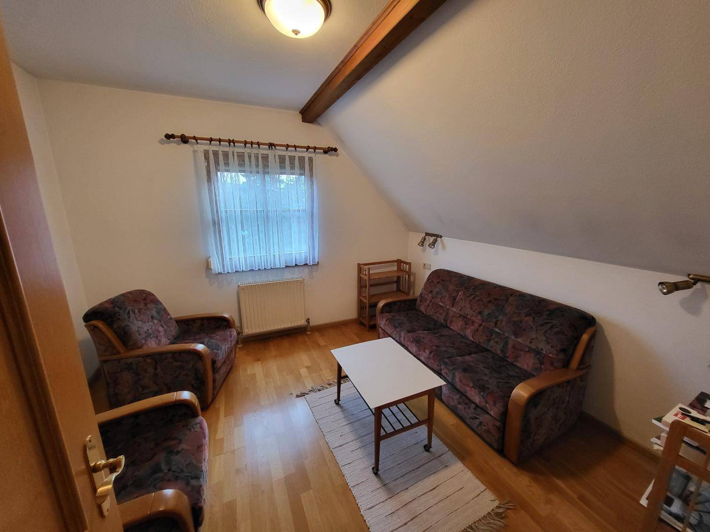 Gemütlicher Wohnbereich im Dachgeschoss mit Sofa, Sessel und Holzboden.