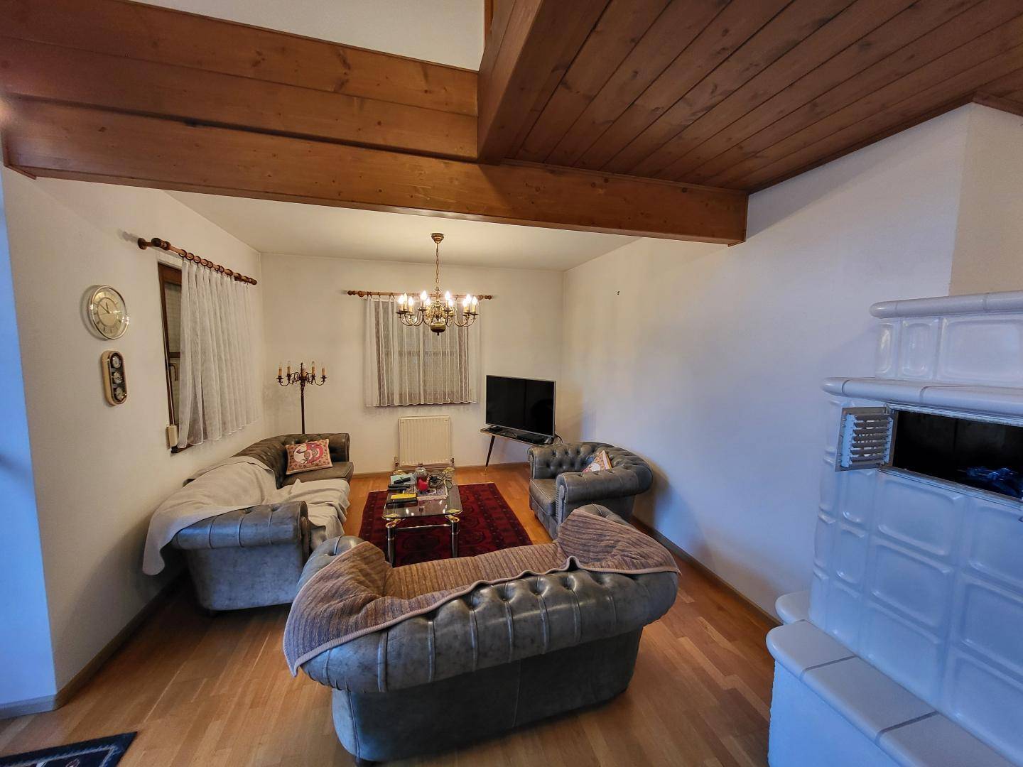 Geräumiges Wohnzimmer mit Kachelofen, Holzboden und bequemen Ledersofas.