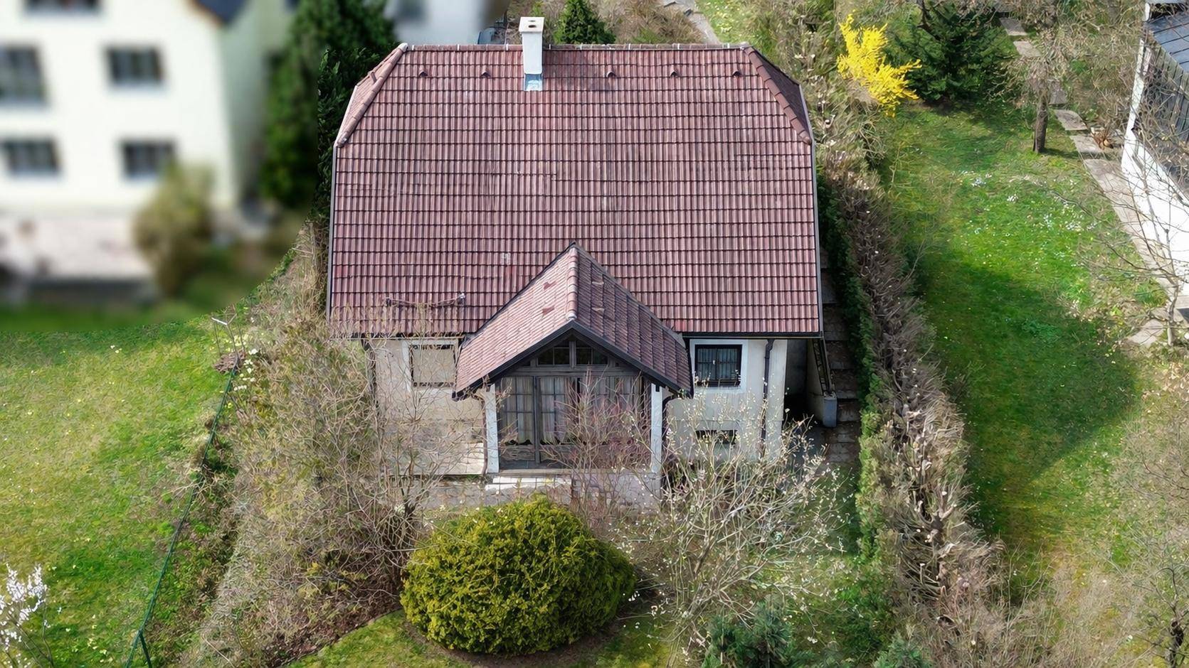 Luftaufnahme eines Einfamilienhauses mit Ziegeldach, umgeben von Bäumen und Grünflächen.
