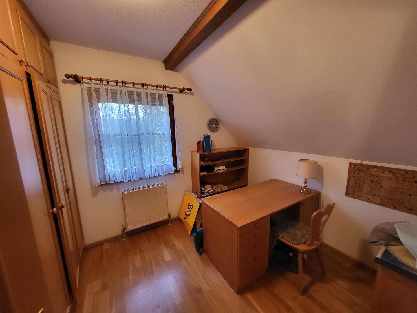 Arbeitszimmer im Dachgeschoss mit Schreibtisch, Schrank und Holzboden.