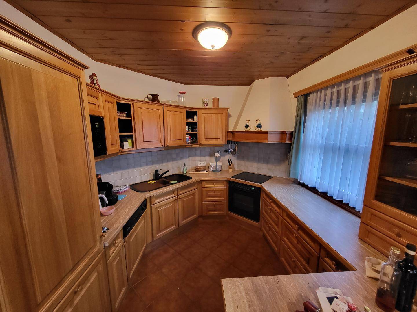 Traditionelle Holzküche mit Einbauschränken, Fliesenboden und Fenster.