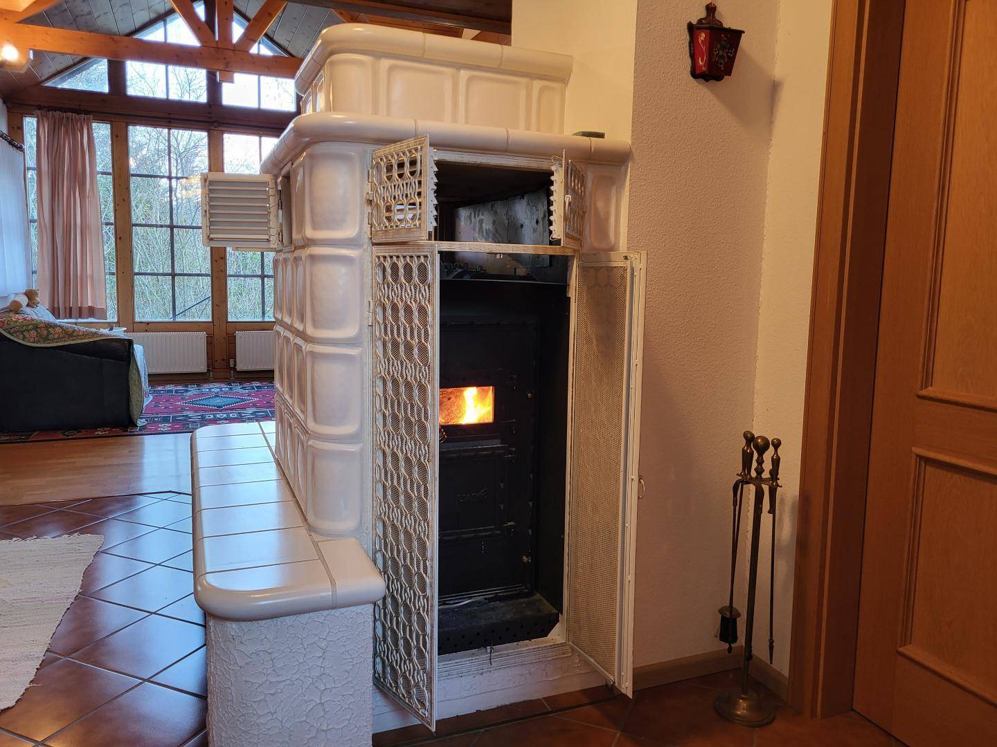 Wohnzimmer mit traditionellem Kachelofen, Holzboden und großen Fenstern.