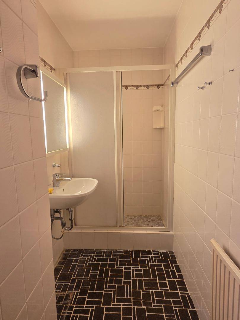 Badezimmer mit Dusche, Waschbecken und dunklen Bodenfliesen in schlichtem Design.