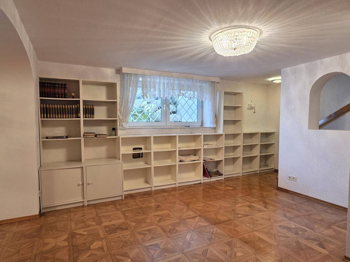 Heller Wohnbereich mit Parkettboden, großen Fenstern und vielen Bücherregalen.