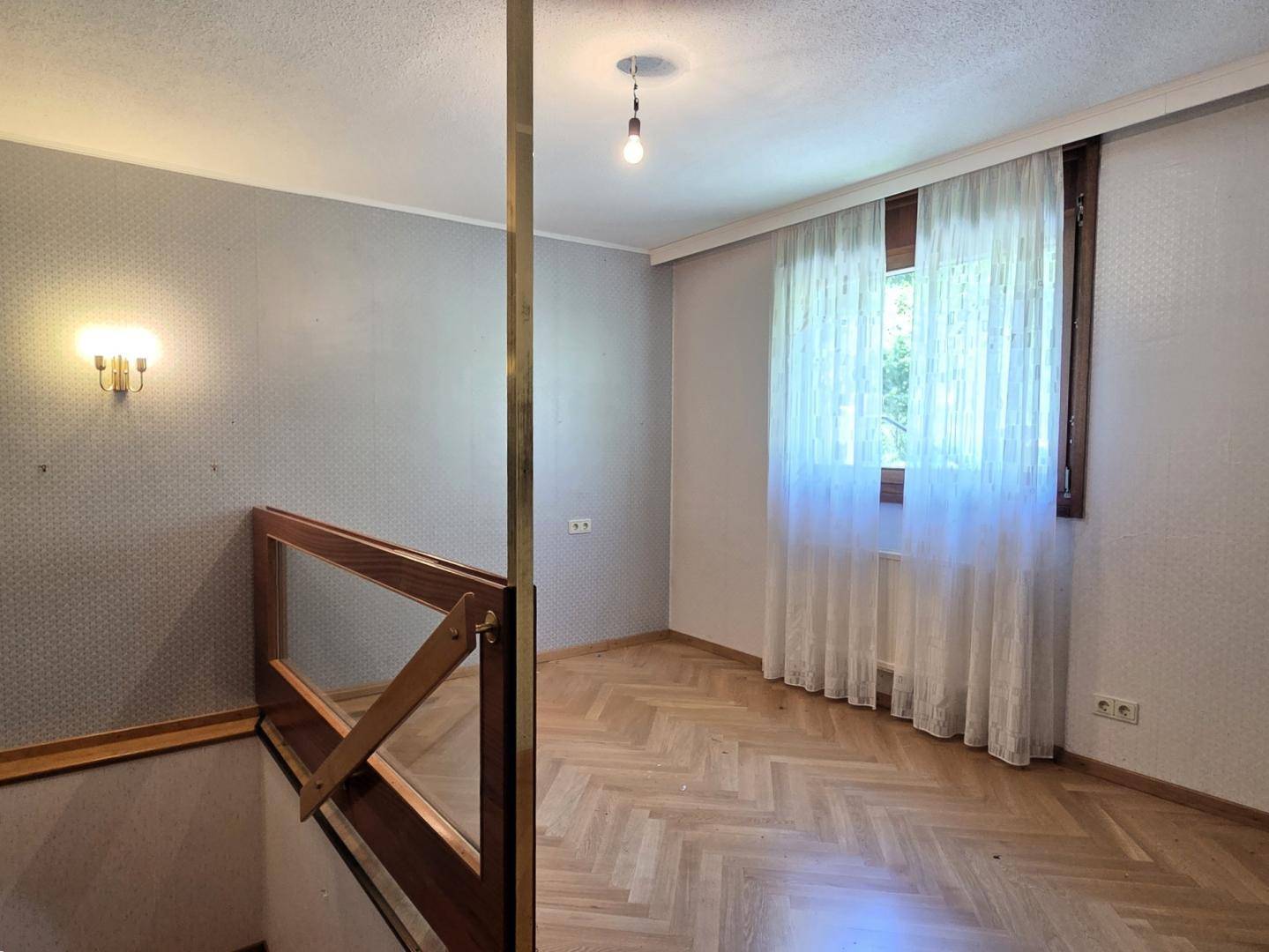 Flur mit Parkettboden, Holzgeländer und Fenster, das Tageslicht hereinlässt.